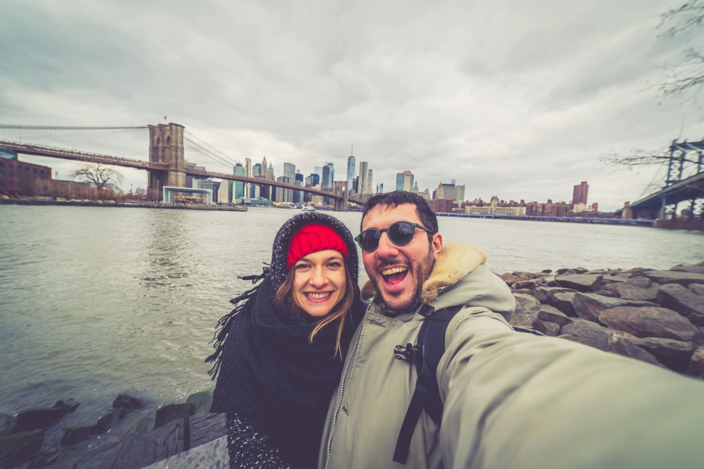 Beau couple heureux prenant un autoportrait en selfie sur le pont de Brooklyn, New York. Touristes branchés s'amusant et photographiant des monuments de New York pour un blog de voyage. Noël d'hiver © photomaticstudio - stock.adobe.com