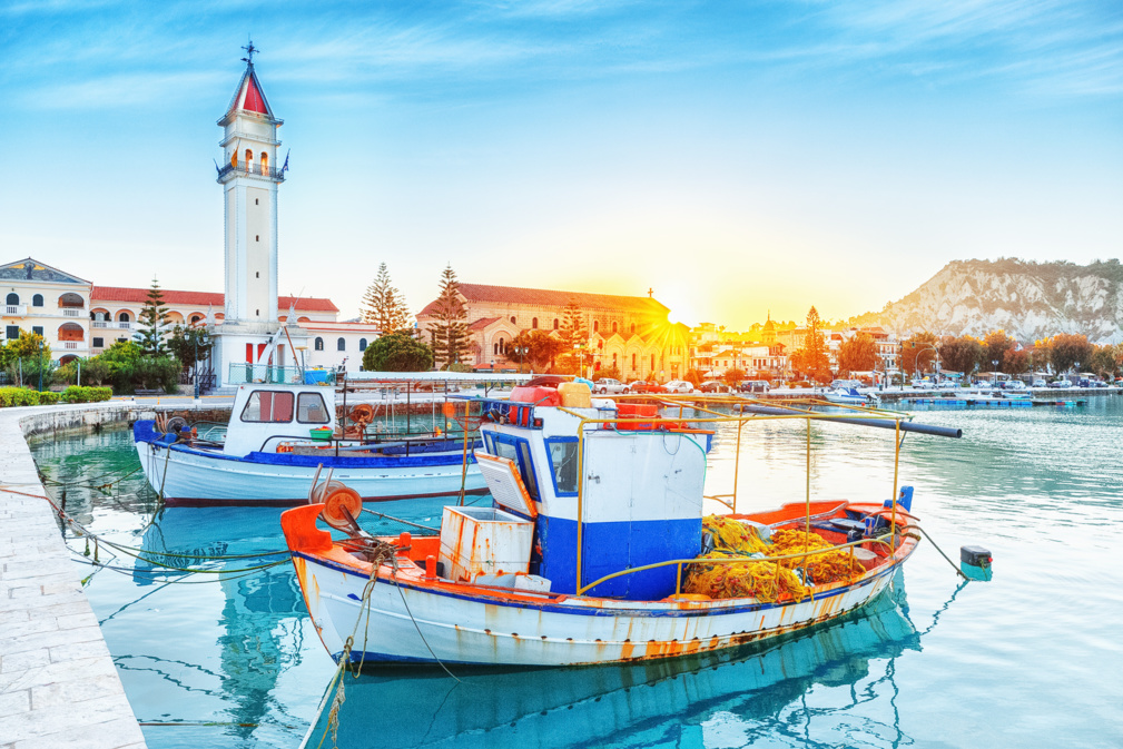 Zante - île de Zakinthos, vieux port avec bateaux amarrés et point de repère de la tour de l'église. Paysage de coucher de soleil majestueux, soleil brillant visible. © Feel good studio - stock.adobe.com