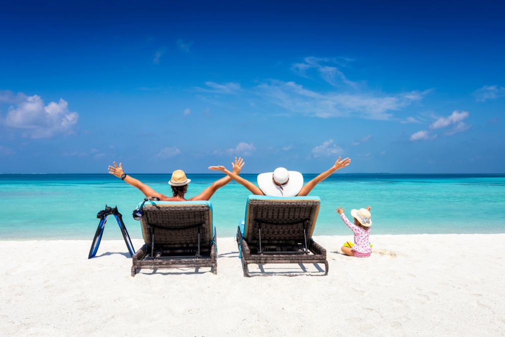 Une famille heureuse sur des chaises longues profite de ses vacances sur une plage tropicale avec un océan turquoise et du soleil. © moofushi - stock.adobe.com