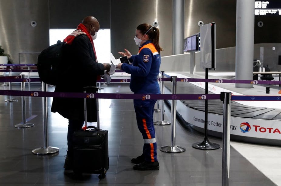 Une membre des services civiques vérifie les documents - dont une attestation de test au Covid négatif - d'un passager au départ de l'aéroport Roissy-Charles de Gaulle le 5 février 2021. Gonzalo Fuentes/AFP