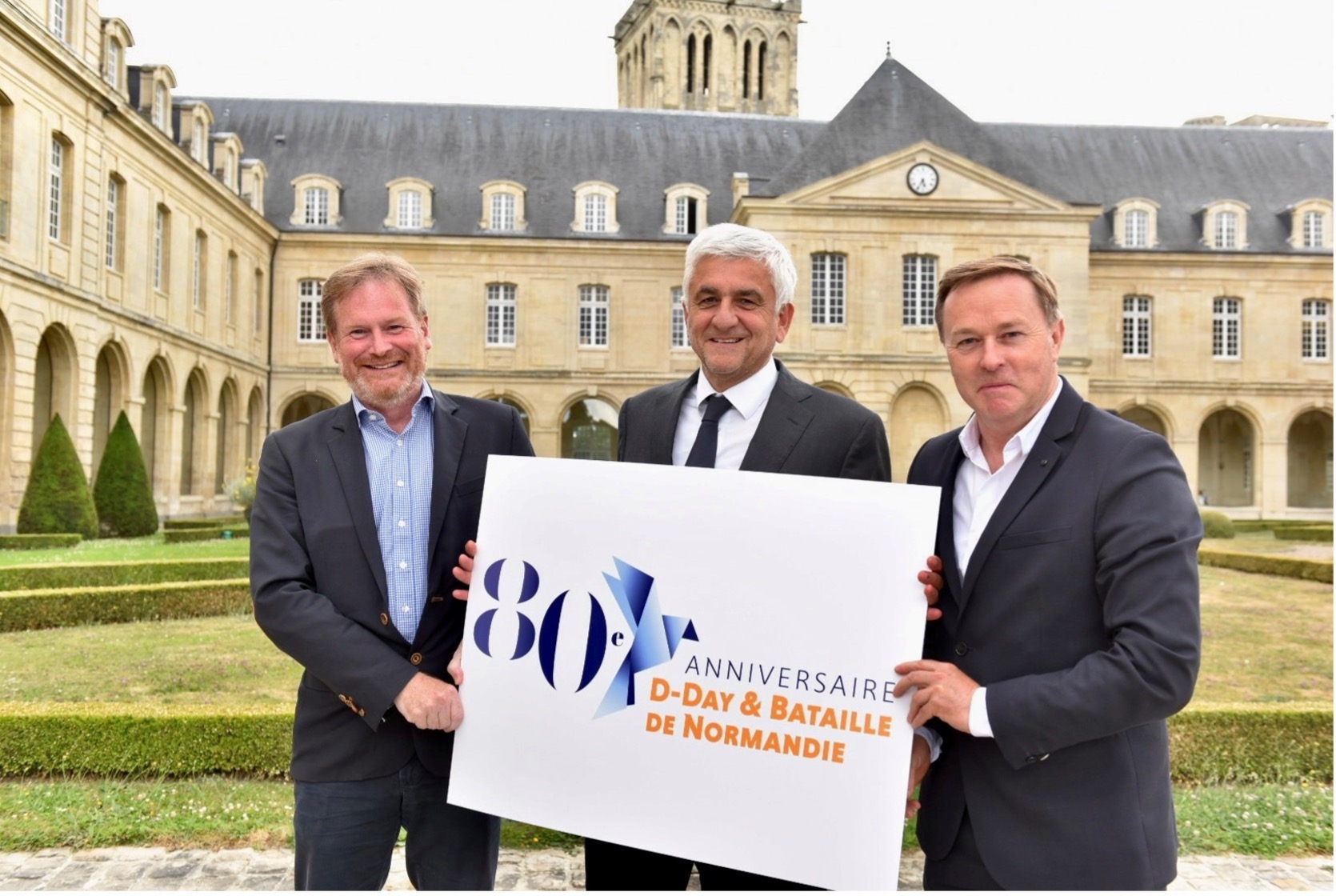 Hervé Morin présente le logo du 80e anniversaire entouré de Loïc Jamin (à D) et Michale Dobbs (à G) (©Normandie Tourisme)